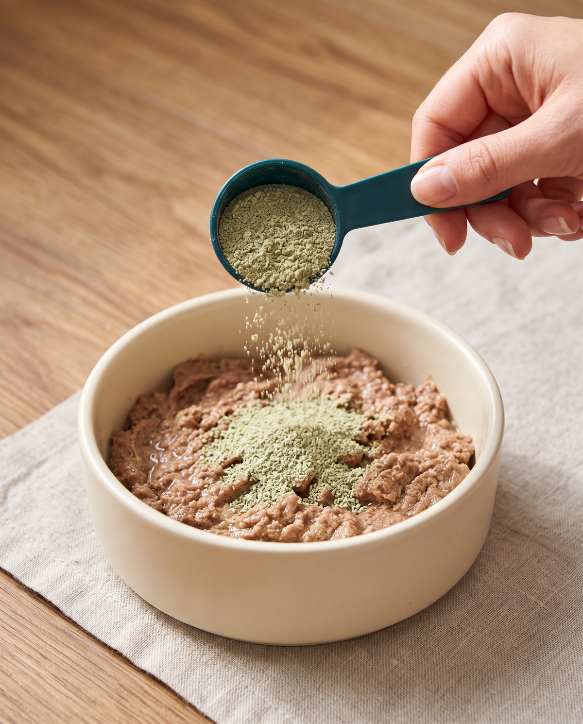 Sprinkling a scoop of NIBBY powder over a bowl of cat food